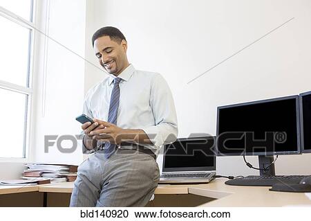 Stock Image - Black businessman using cell phone in office. Fotosearch