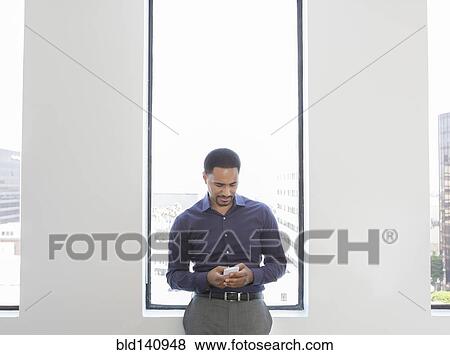 Stock Photo - Black businessman using cell phone in office. Fotosearch