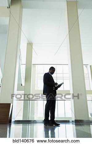 Black businessman using digital tablet in office hallway View Large Photo Image Stock Photograph - Black businessman using digital tablet in office hallway. Fotosearch