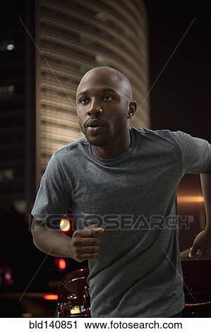 Stock Image - Black man running in city at night. Fotosearch