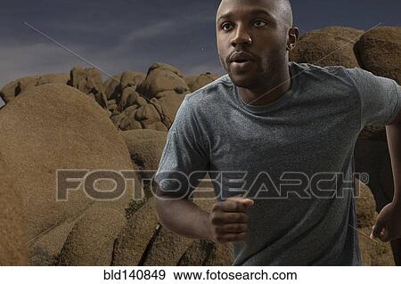 Stock Photo - Black man running in rocky remote landscape. Fotosearch