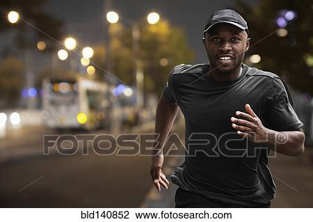 Stock Image - Black man running on city street at night. Fotosearch