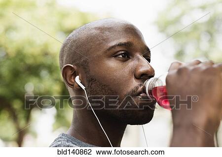 Stock Image - Black runner drinking juice in city with earbuds. Fotosearch