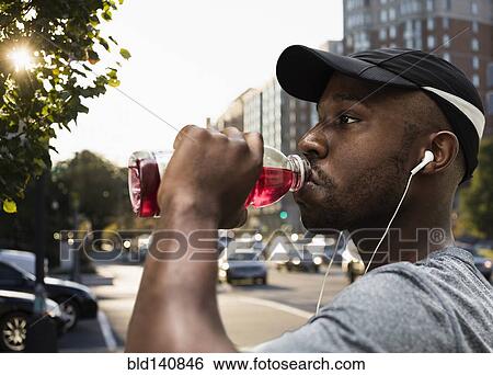 Stock Photograph - Black runner drinking juice in city. Fotosearch