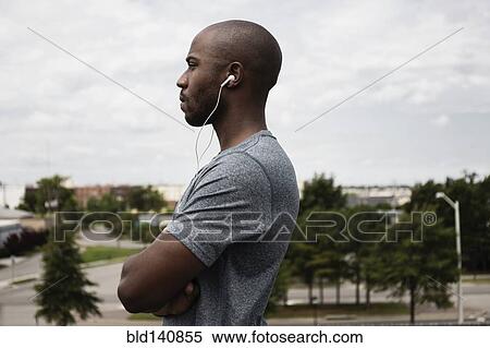 Stock Photography - Black runner listening to earbuds in urban park. Fotosearch
