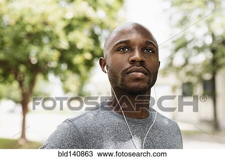 Stock Image - Black runner resting in park with earbuds. Fotosearch