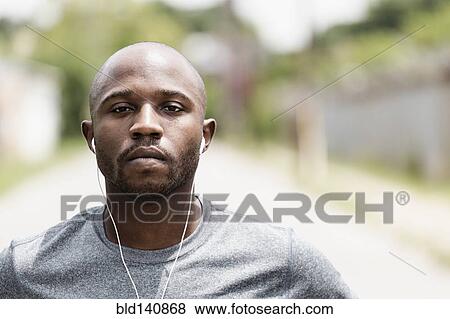 Stock Photo - Black runner resting on city street with earbuds. Fotosearch
