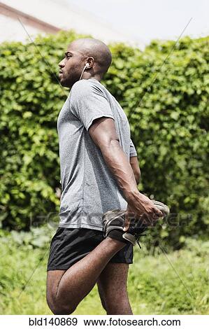 Stock Photo - Black runner with earbuds stretching leg . Fotosearch