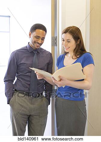 Stock Image - Business people reading folder in office hallway. Fotosearch