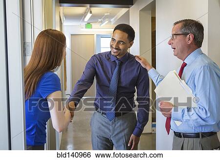 Stock Photograph - Business people shaking hands in office hallway. Fotosearch