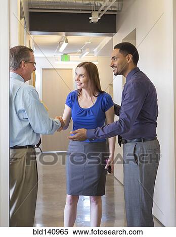 Stock Photography - Business people shaking hands in office hallway. Fotosearch