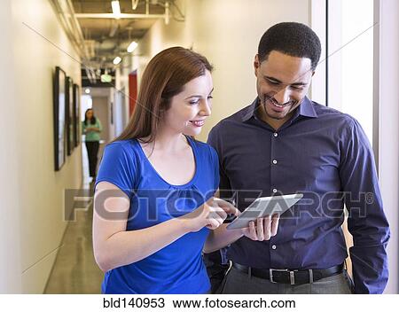 Stock Image - Business people using digital tablet in office hallway. Fotosearch