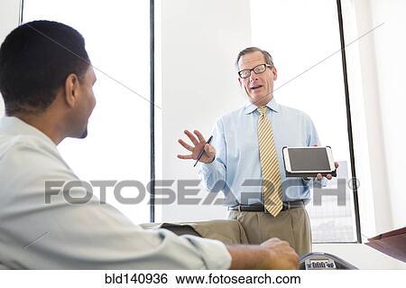 Stock Photograph - Businessman showing digital tablet to colleagues in meeting. Fotosearch