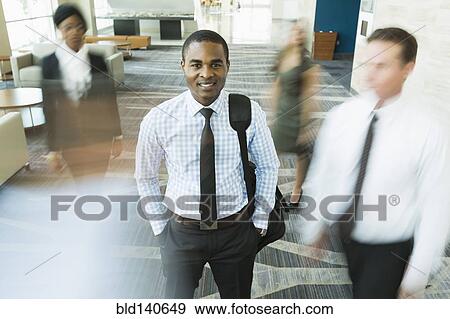 Stock Photo - Businessman standing still in busy office lobby. Fotosearch