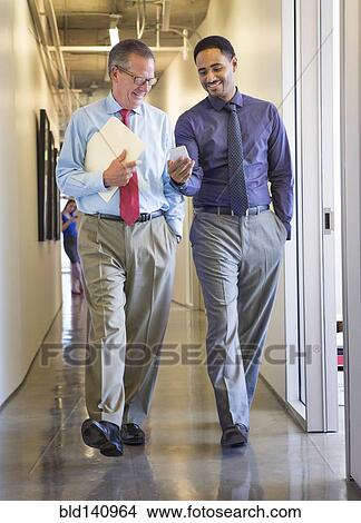 Picture - Businessmen using cell phone in office hallway. Fotosearch