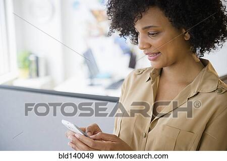 Stock Photo - Businesswoman using cell phone in cubicle. Fotosearch