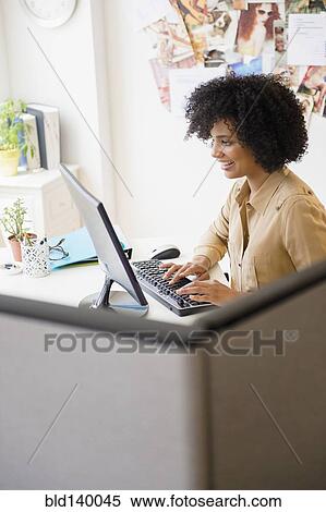 Stock Photography - Businesswoman working at computer in cubicle. Fotosearch