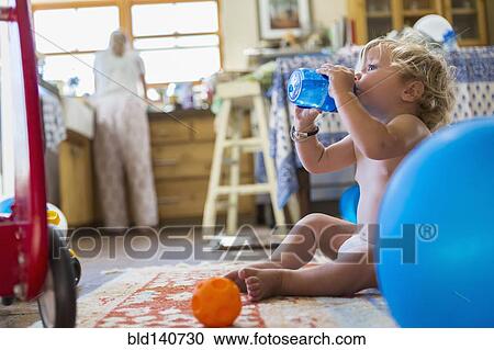 Stock Image - Caucasian baby boy drinking water in kitchen. Fotosearch