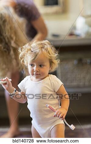 Stock Photo - Caucasian baby boy holding toothbrush in bathroom. Fotosearch