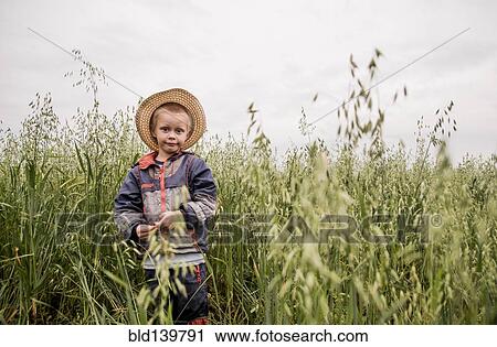 Stock Image - Caucasian boy standing in tall grass in rural field. Fotosearch
