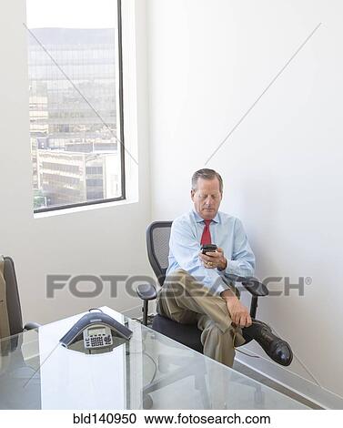 Stock Image - Caucasian businessman using cell phone at desk in office. Fotosearch