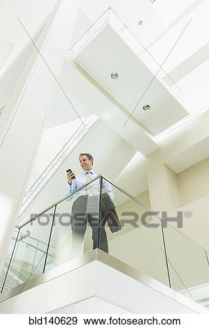 Stock Photo - Caucasian businessman using cell phone on office balcony. Fotosearch