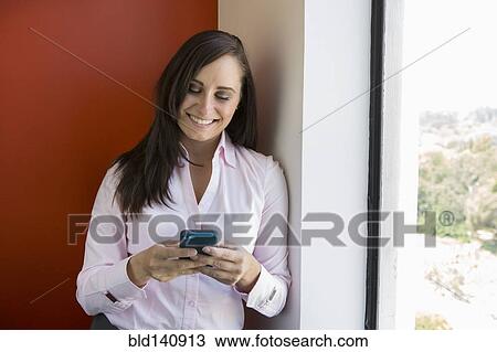 Stock Image - Caucasian businesswoman using cell phone near window. Fotosearch