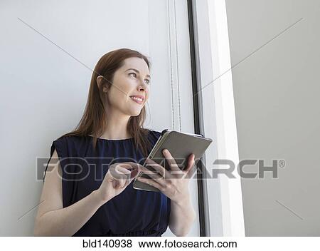 Stock Photo - Caucasian businesswoman using digital tablet at office window. Fotosearch