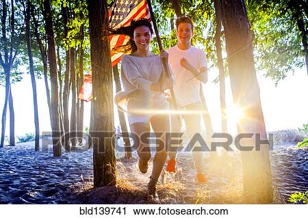 Caucasian couple carrying American flag in trees on beach View Large Photo Image Stock Image - Caucasian couple carrying American flag in trees on beach. Fotosearch