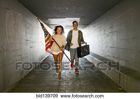 Caucasian couple carrying American flag and boom box in tunnel View Large Photo Image Stock Photo - Caucasian couple carrying American flag and boom box in tunnel. Fotosearch