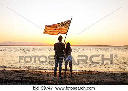 Stock Photo - Caucasian couple holding American flag on beach. Fotosearch