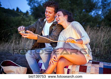 Stock Image - Caucasian couple making smores on log. Fotosearch