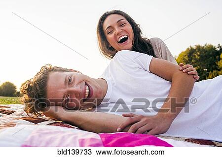 Stock Image - Caucasian couple relaxing on blankets in park. Fotosearch