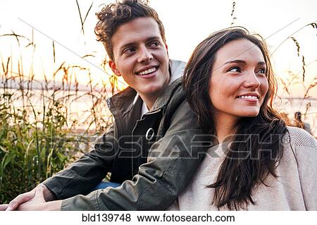 Stock Photo - Caucasian couple sitting together on beach. Fotosearch