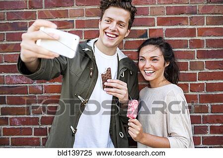 Caucasian couple taking selfie near red brick wall View Large Photo Image Stock Photography - Caucasian couple taking selfie near red brick wall. Fotosearch