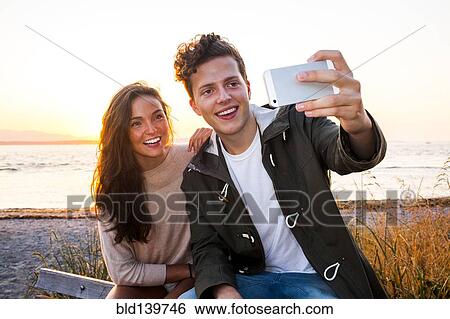 Stock Photograph - Caucasian couple taking selfie on beach. Fotosearch