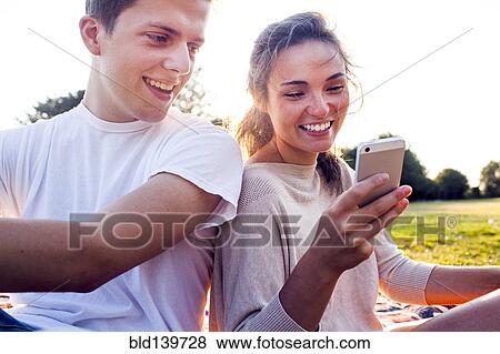 Stock Photo - Caucasian couple using cell phone outdoors. Fotosearch