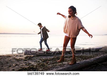 Caucasian couple walking on logs on beach View Large Photo Image Stock Photo - Caucasian couple walking on logs on beach. Fotosearch