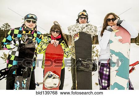 Stock Photo - Caucasian couples holding snowboards in snow. Fotosearch