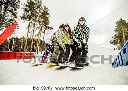 Stock Photo - Caucasian couples snowboarding together on snowy hill. Fotosearch