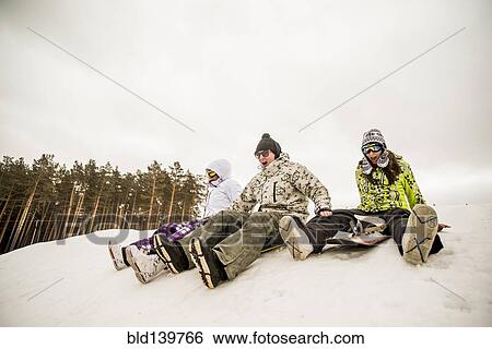 Stock Photograph - Caucasian friends sitting on snowboards. Fotosearch