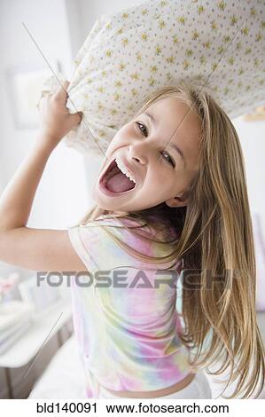Stock Image - Caucasian girl having pillow fight in bedroom. Fotosearch