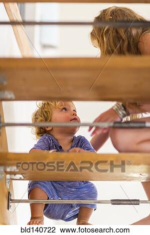 Stock Image - Caucasian girl helping baby brother on staircase. Fotosearch