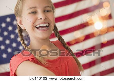 Stock Image - Caucasian girl holding sparkler by American flag. Fotosearch