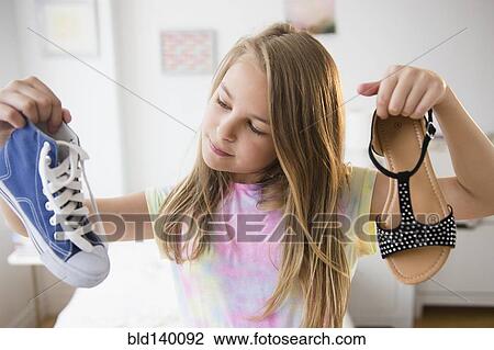 Stock Image - Caucasian girl picking shoes in bedroom. Fotosearch