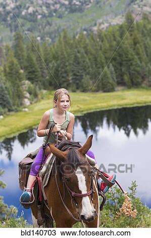 Stock Image - Caucasian girl riding horse in near lake. Fotosearch