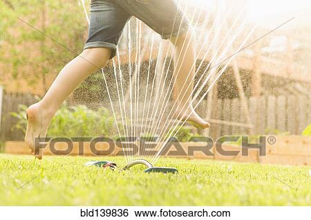 Stock Photograph - Caucasian girl running through sprinkler in backyard. Fotosearch