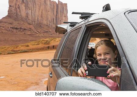 Stock Photo - Caucasian girl taking cell phone photograph from car, Monument Valley, Utah, United States. Fotosearch