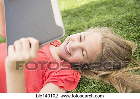 Stock Image - Caucasian girl using digital tablet on grassy lawn. Fotosearch