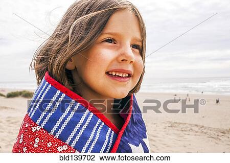 Stock Image - Caucasian girl wrapped in blanket on beach. Fotosearch